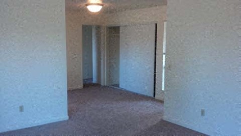 A room with a carpet floor and a doorway leading to another room.