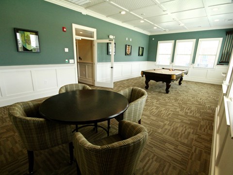 A room with a pool table and chairs.