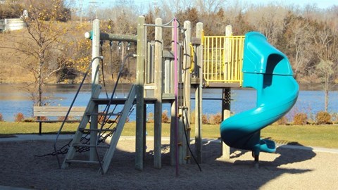 a playground with a blue slide next to a lake
