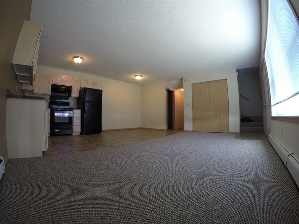 an empty living room with a kitchen and a large window