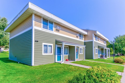 the exterior of two houses with green and brown siding and a green lawn
