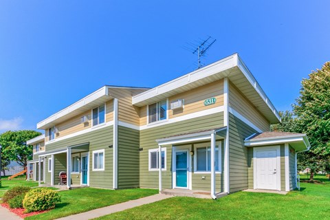the front of a green house with a lawn and a blue sky