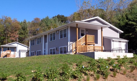 a gray house with a wooden porch on a hill