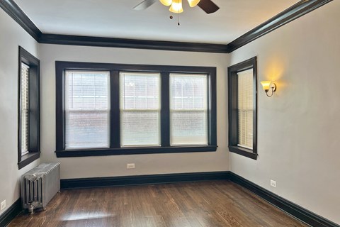 A room with a ceiling fan, two windows, and a radiator.