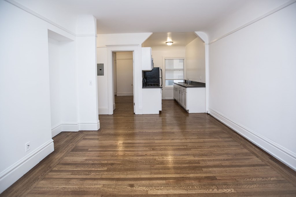 a renovated living room and kitchen with a wood floor and white walls