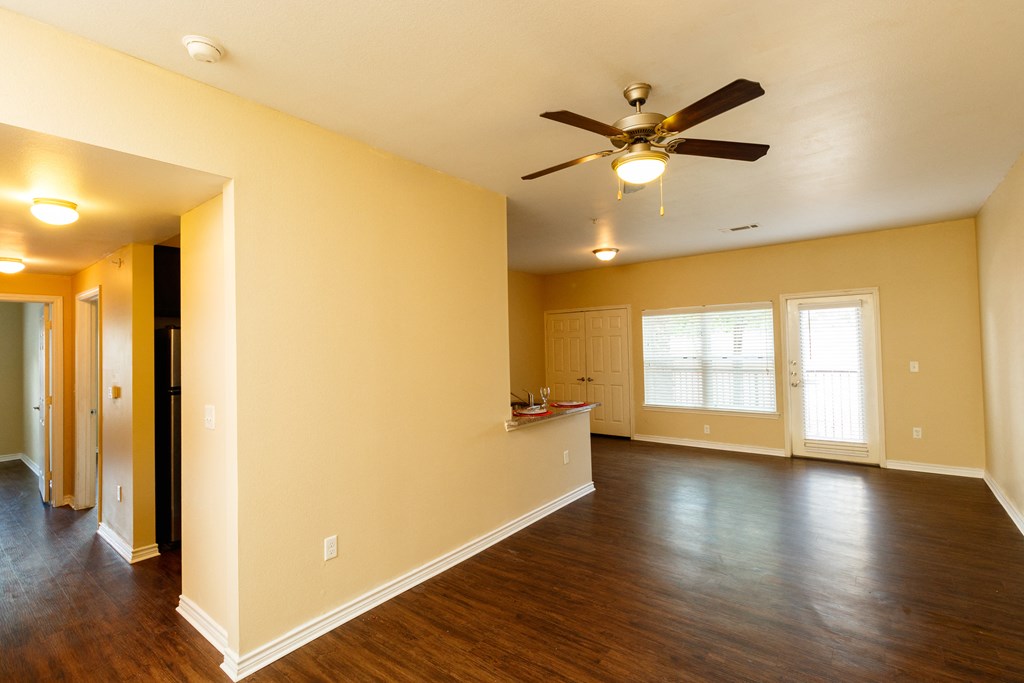 an empty living room with a ceiling fan and a kitchen