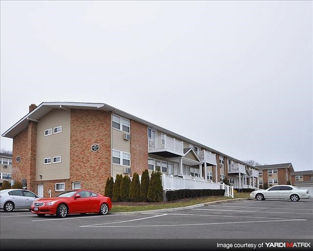 A red car is parked in a parking lot in front of apartment buildings.