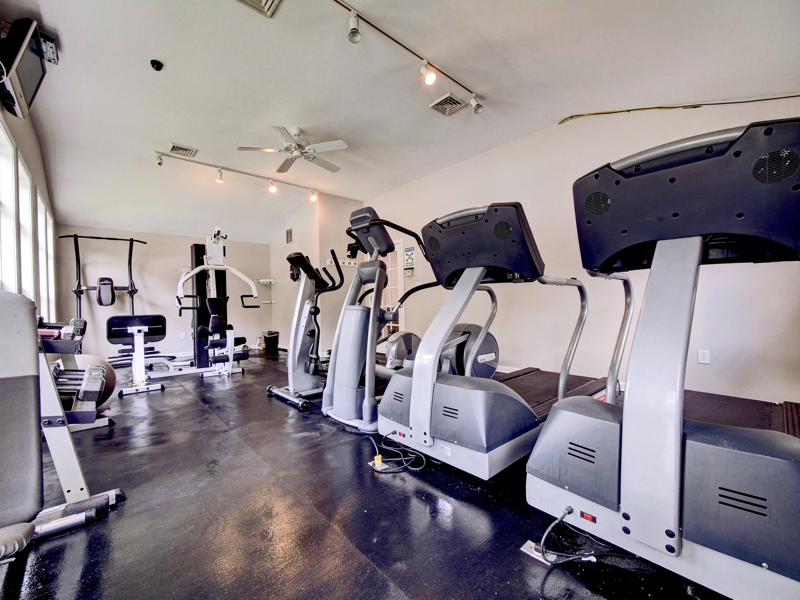 a gym with cardio machines and a ceiling fan