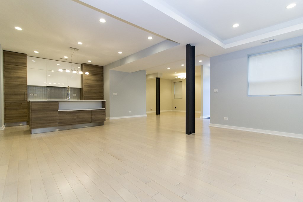 an empty living room with a kitchen in the background