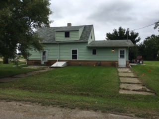 a green house with a porch and a green lawn