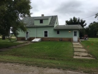 a green house with a porch and a green lawn