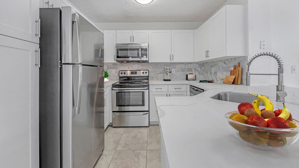 a white kitchen with stainless steel appliances and a bowl of fruit