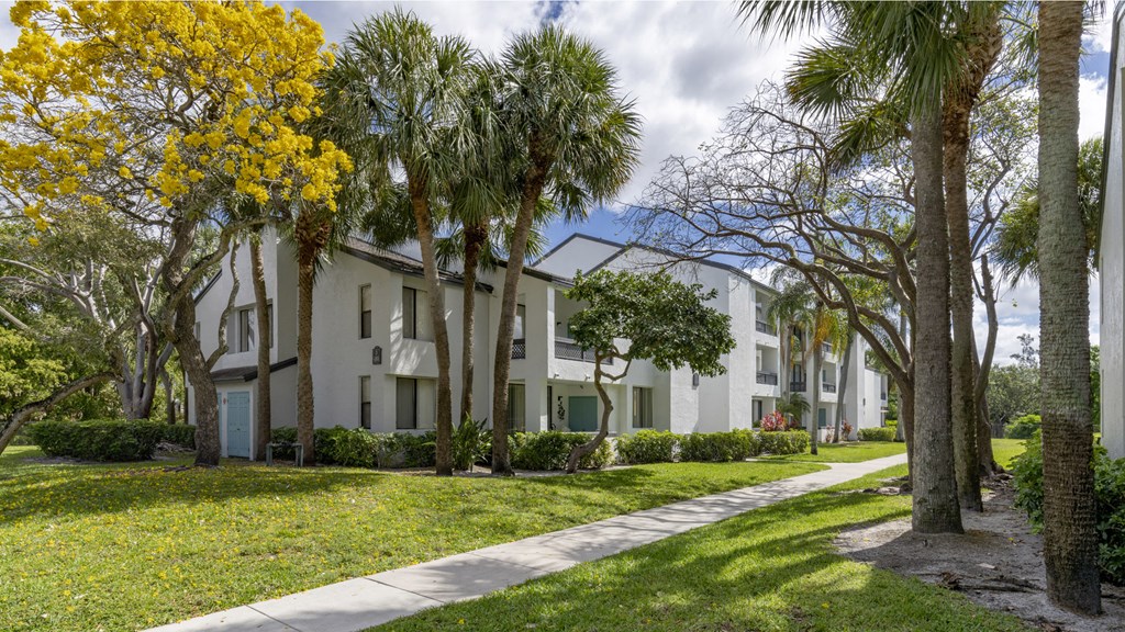 an apartment building with palm trees and a sidewalk