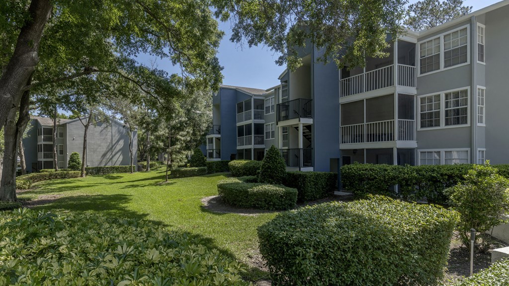 an exterior view of an apartment building with a lawn and trees
