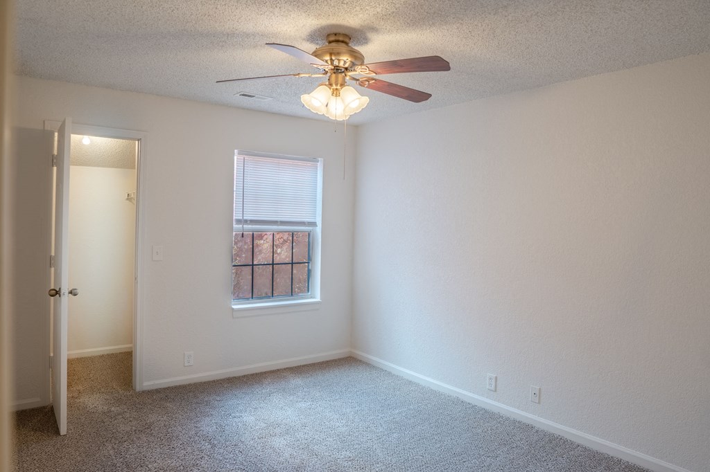 A room with a ceiling fan and a window with a view of a building outside.