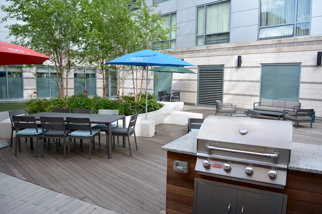 a patio with a grill and a table with chairs and umbrellas