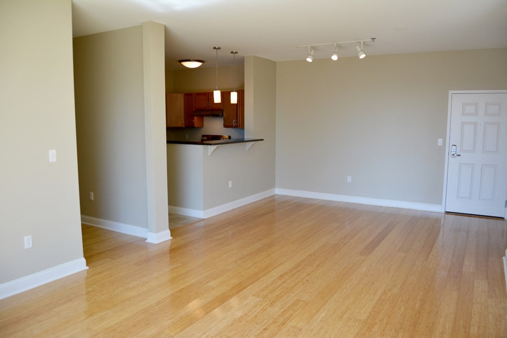 an empty living room with wood floors and a kitchen