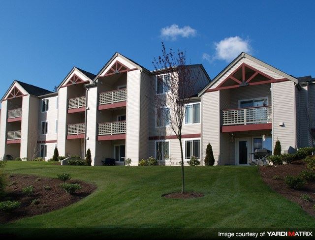 an apartment building with a green lawn and a tree