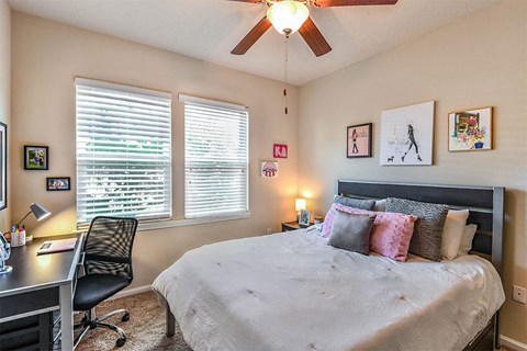 a bedroom with a bed and a desk and a ceiling fan