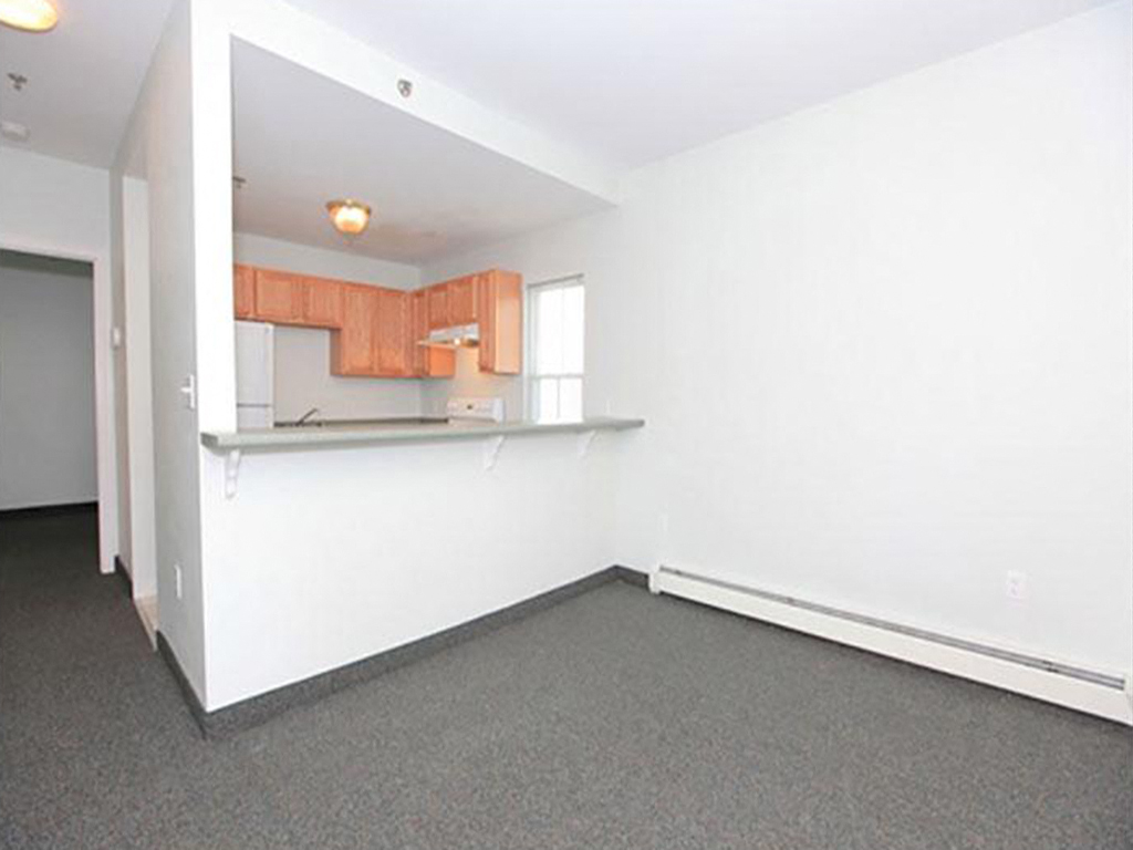 an empty living room with a white wall and a kitchen