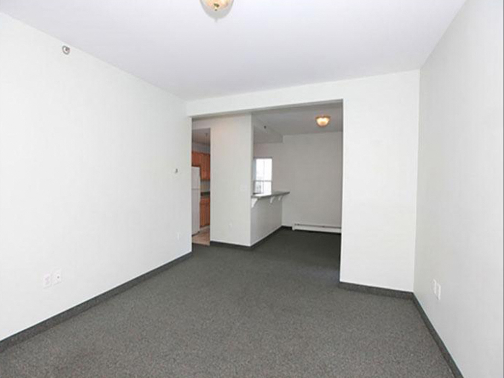 an empty living room with a kitchen in the background