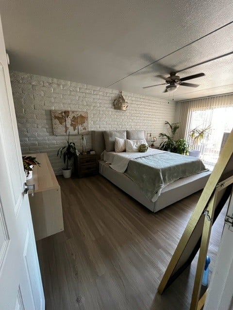 A bedroom with a bed, a ceiling fan, and a white brick wall.