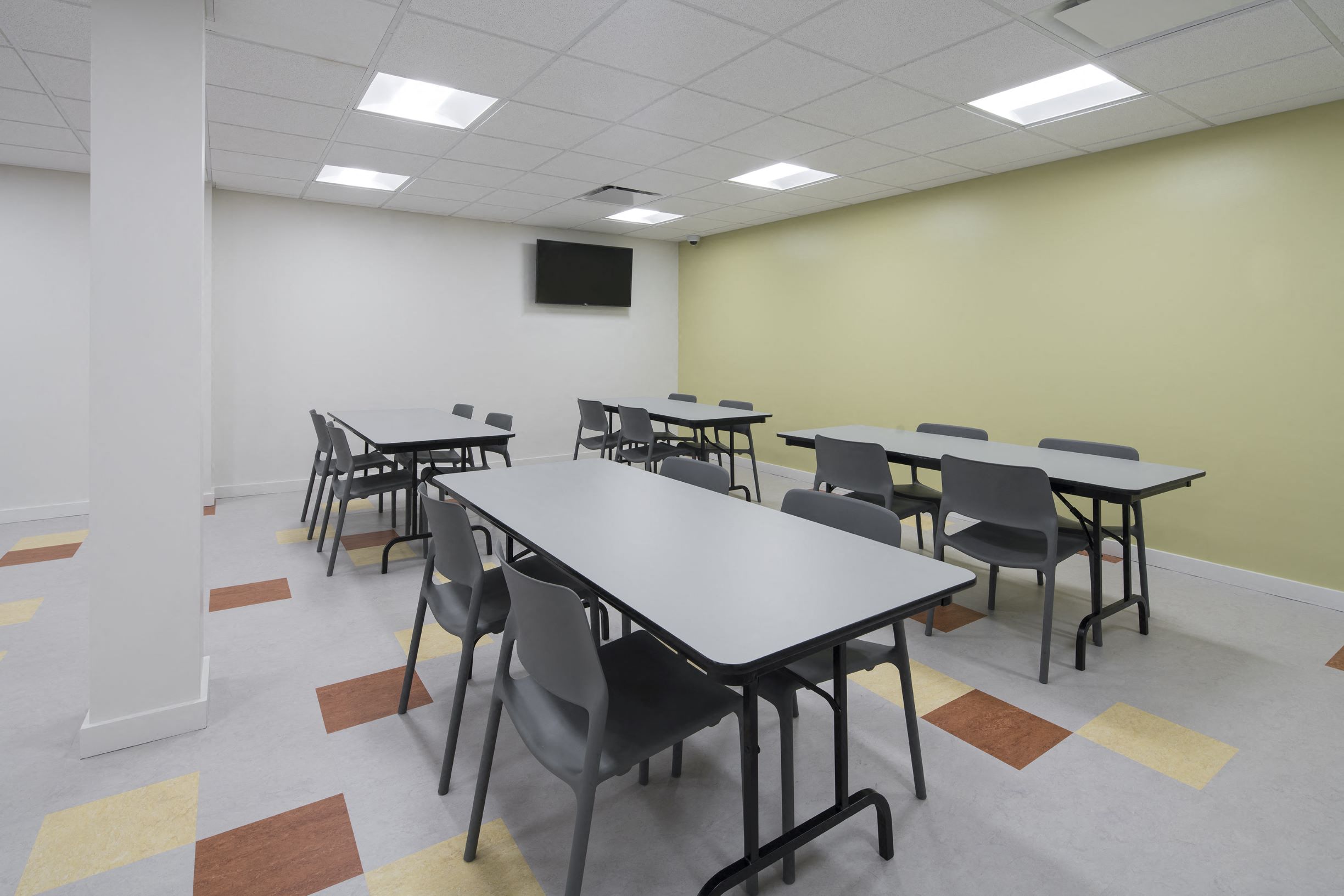 a classroom room with tables and chairs and a tv