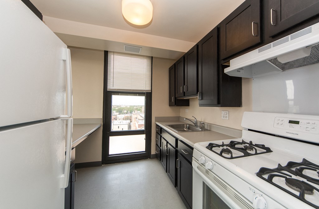 a kitchen with white appliances and black cabinets and a door to a balcony