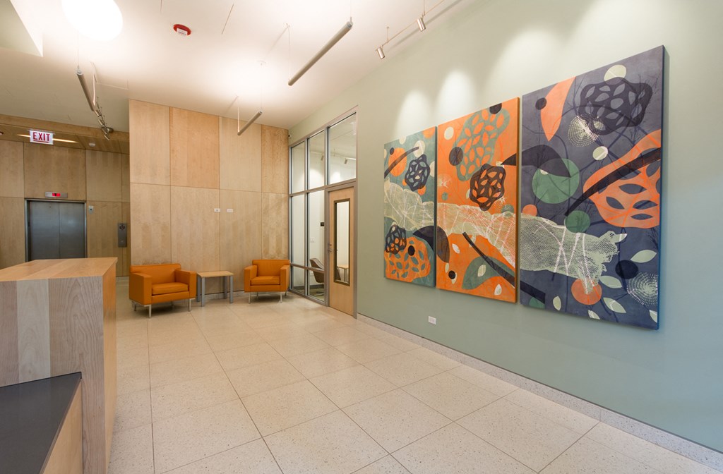 a lobby with a painting on the wall and orange chairs