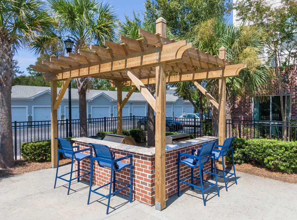 a brick bar with blue chairs under a wooden pergola