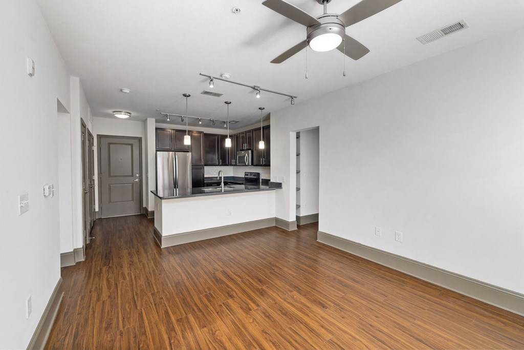 an empty living room and kitchen with wood flooring and a ceiling fan