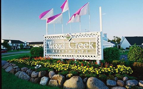 a sign for wood creek apartments with flags on top of it