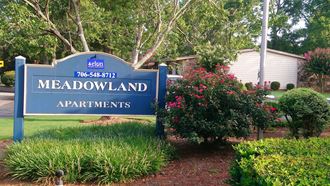 a sign for the meadowland apartments in front of a garden