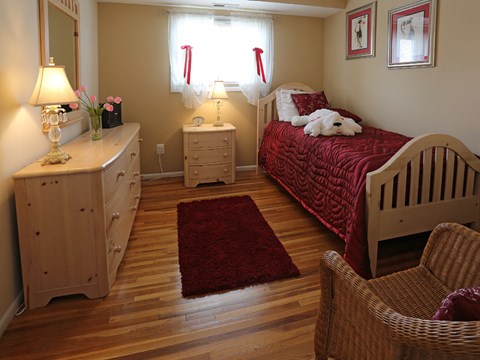 A bedroom with a red rug and a white teddy bear on the bed.