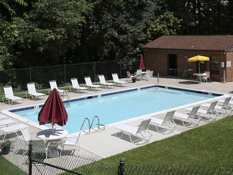 A pool with chairs and umbrellas is surrounded by a fence.