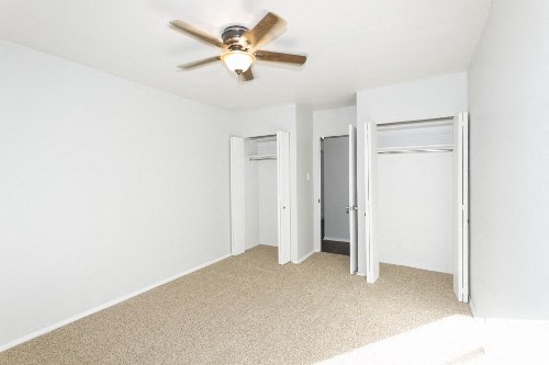 an empty living room with a ceiling fan and closet