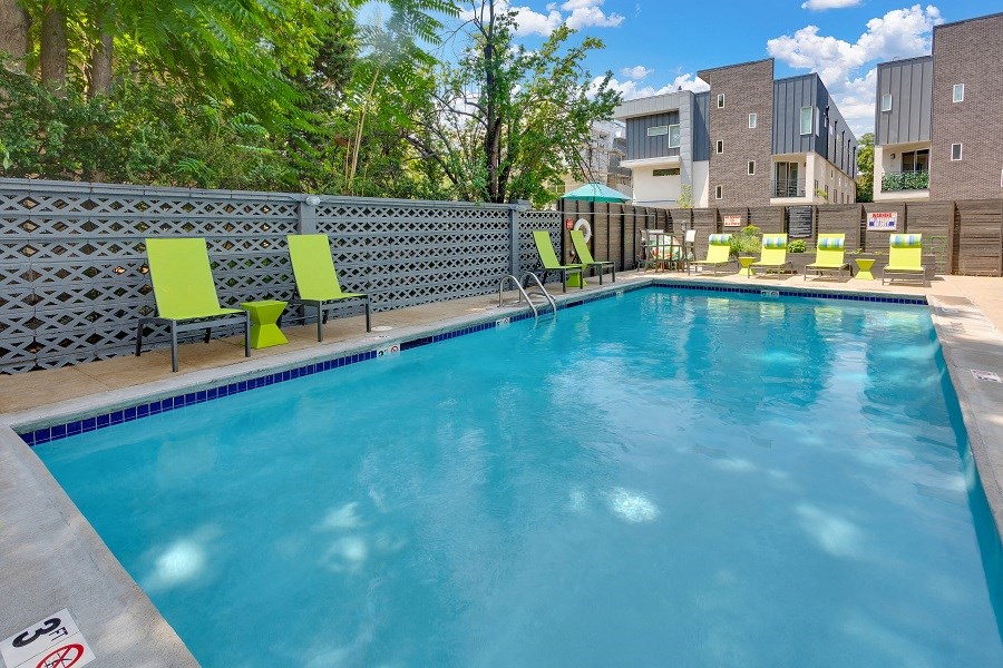 a swimming pool with green chairs and a building in the background
