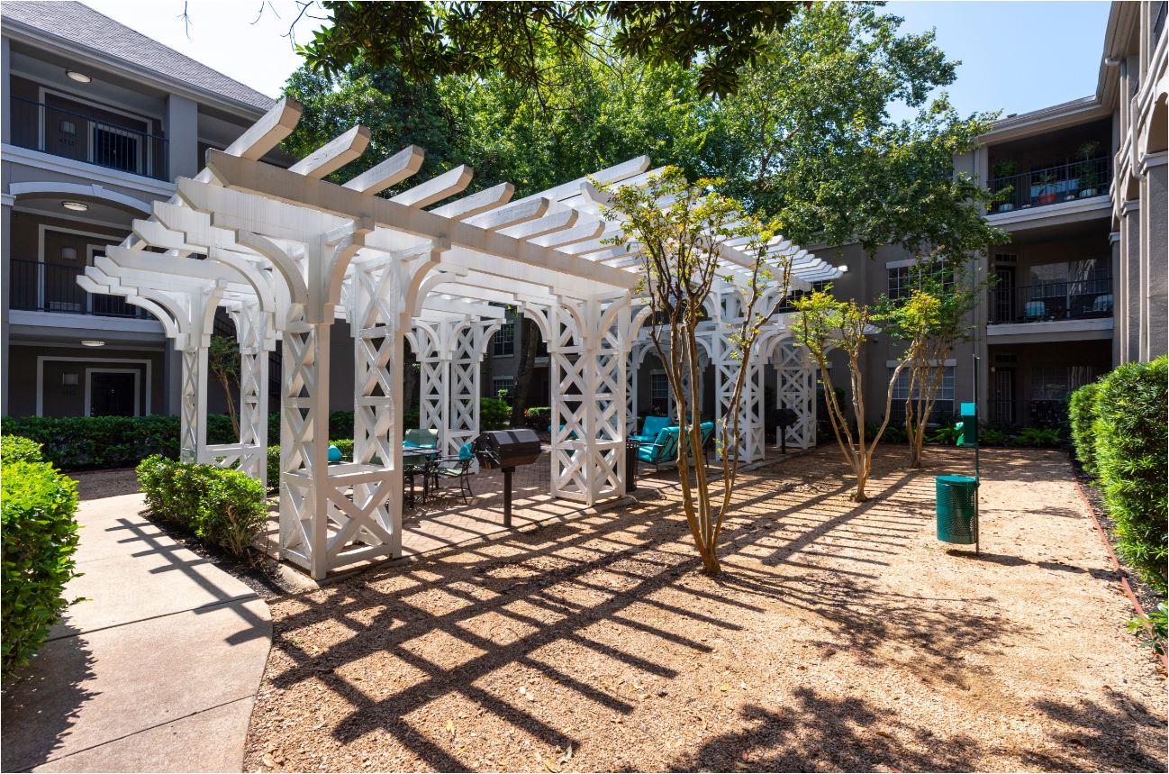 a patio with a white pergola and some trees in front of a building