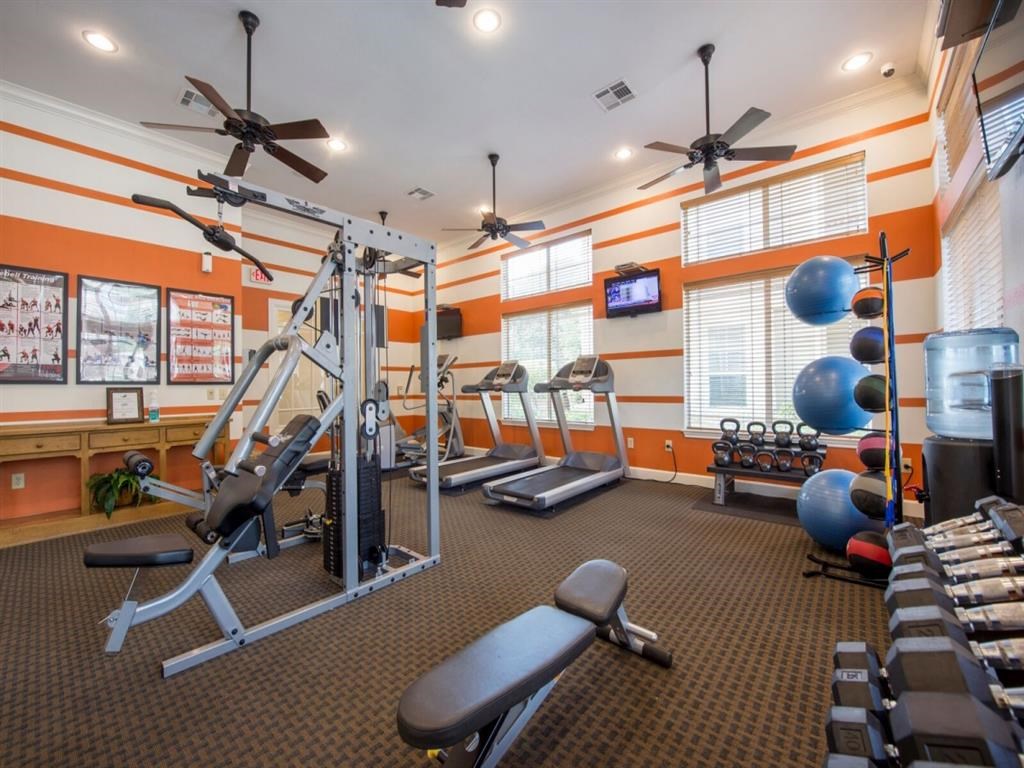 a gym with weights and cardio equipment and a tv