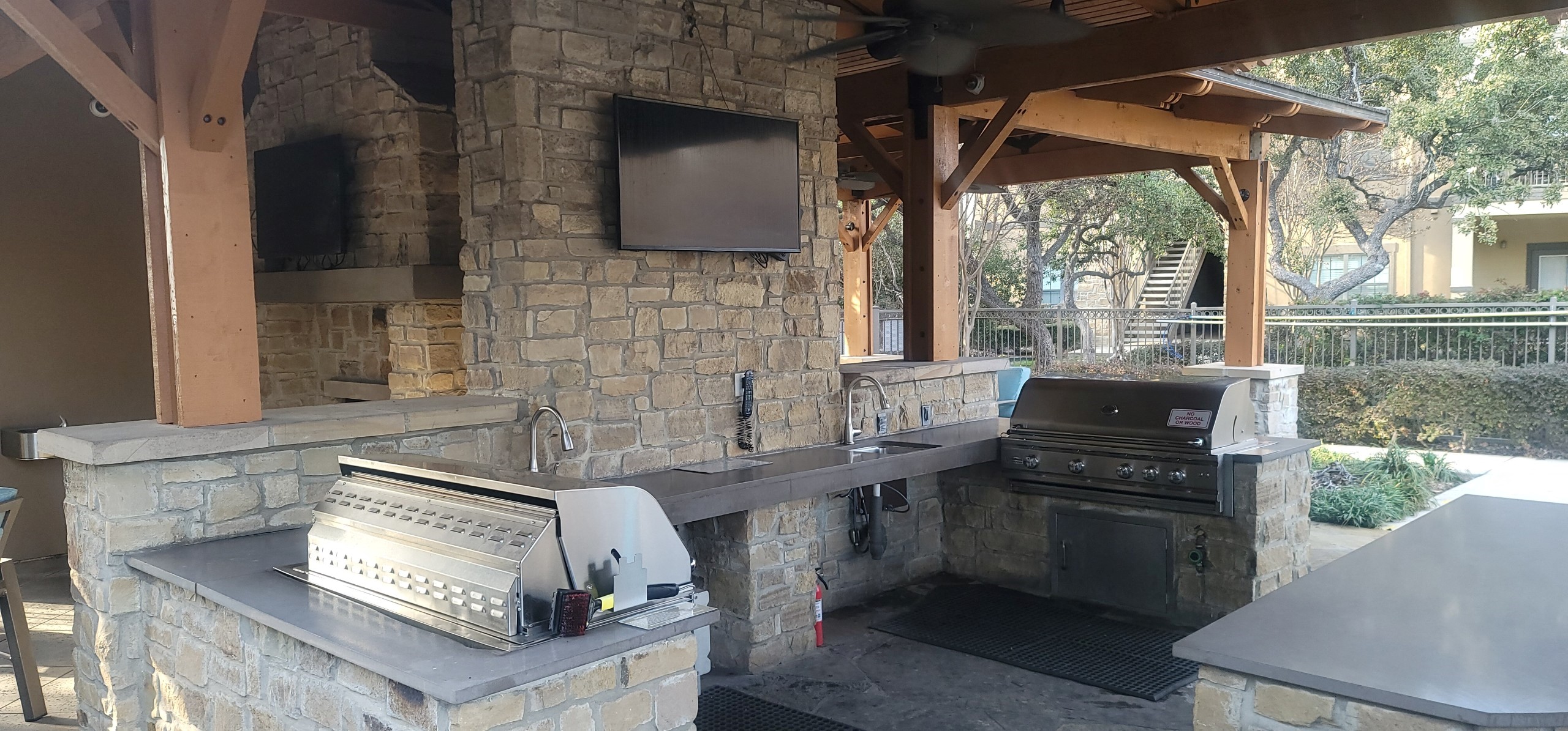 a outdoor kitchen with a grill and a television on a stone wall