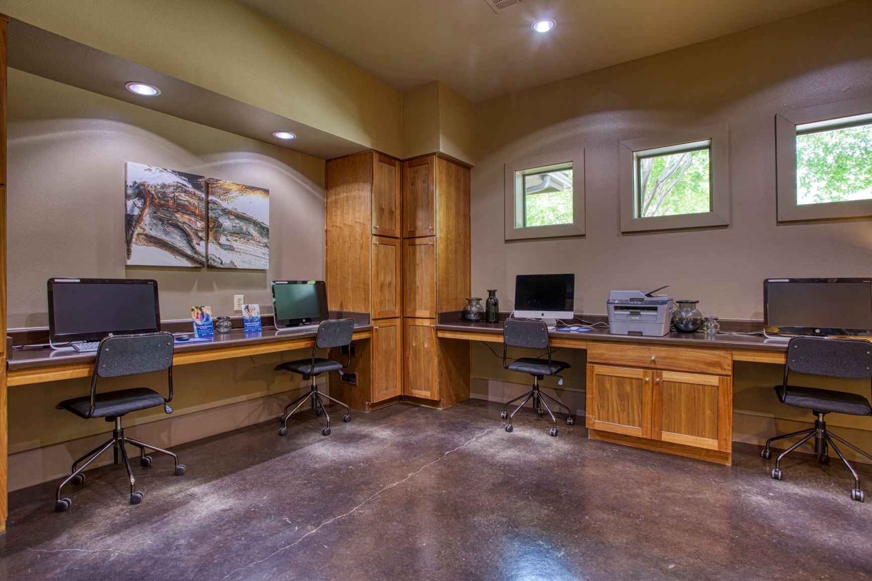 two computer desks and three chairs in a room with windows