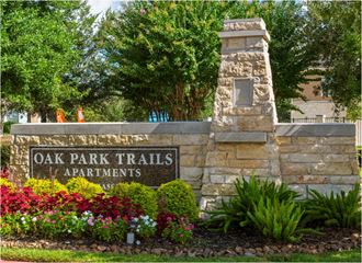 a sign for oak park trails apartments in front of a stone wall and flowers