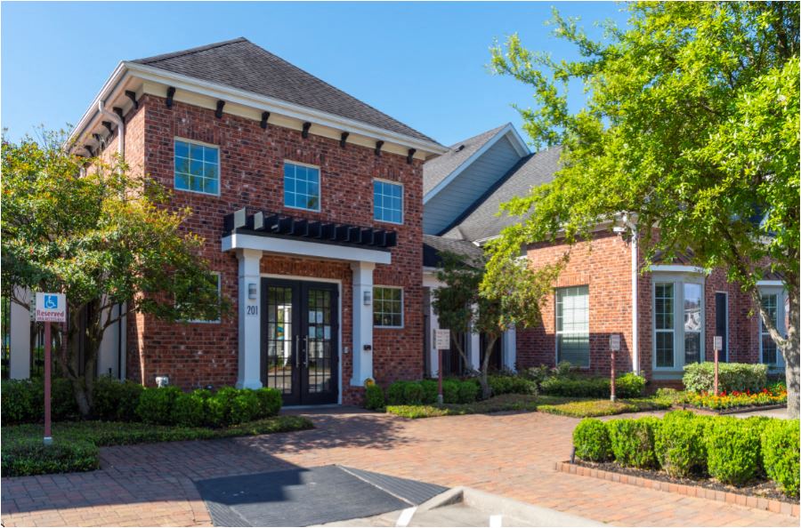 the front of a brick house with a driveway and trees