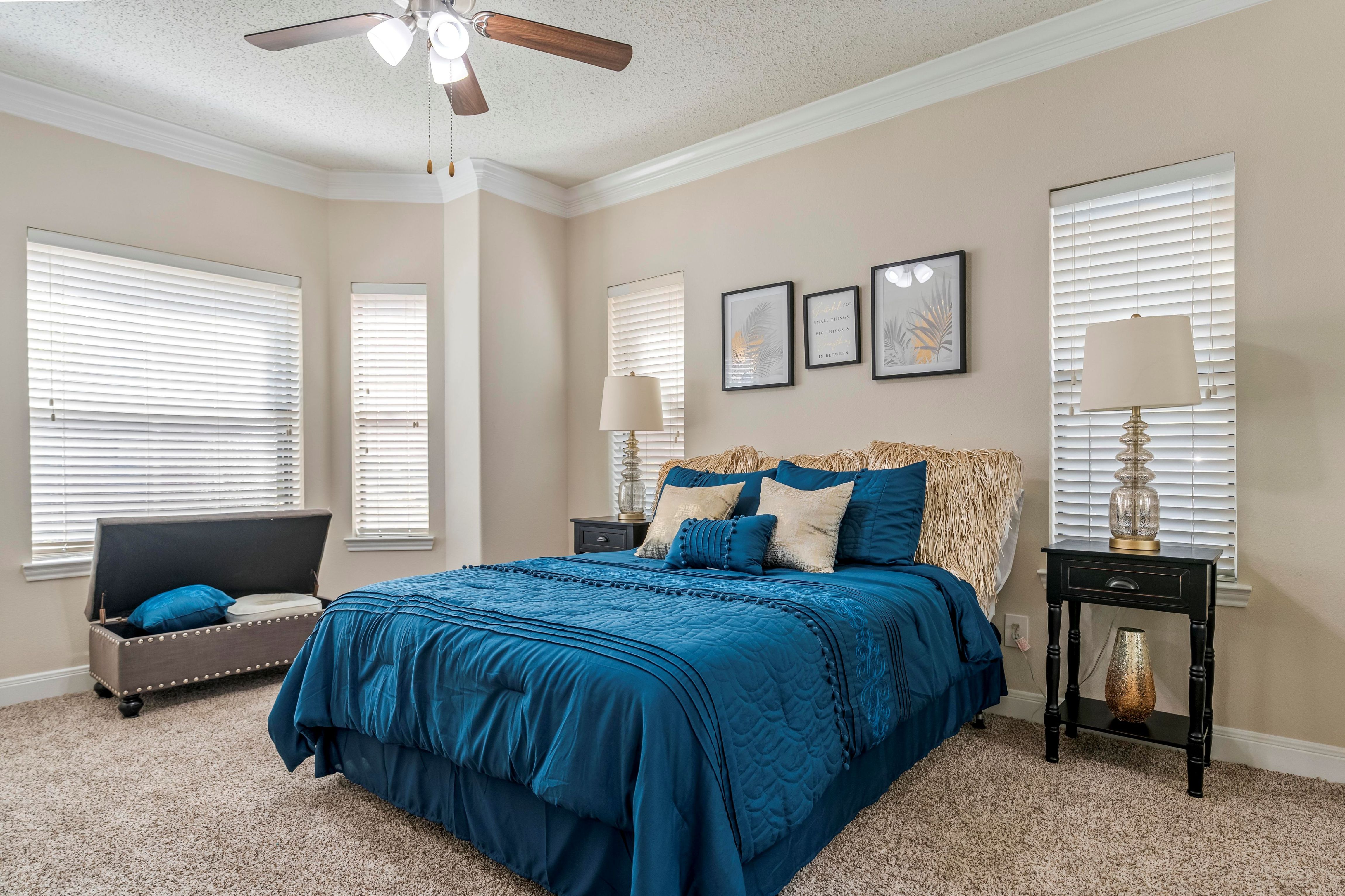 A bedroom with a blue bedspread and a ceiling fan.