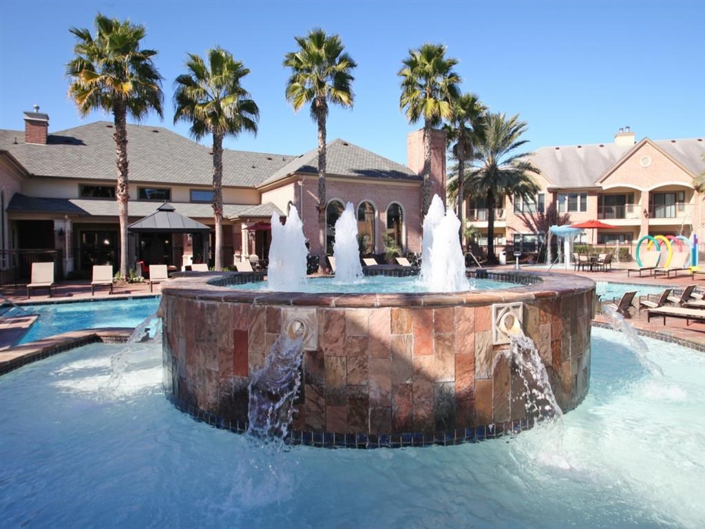 a fountain in the middle of a swimming pool with palm trees