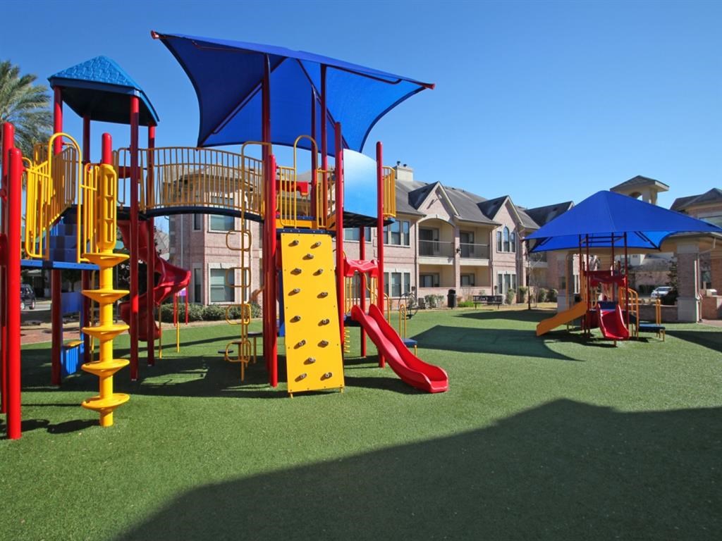 a playground with colorful playsets and umbrellas in front of houses