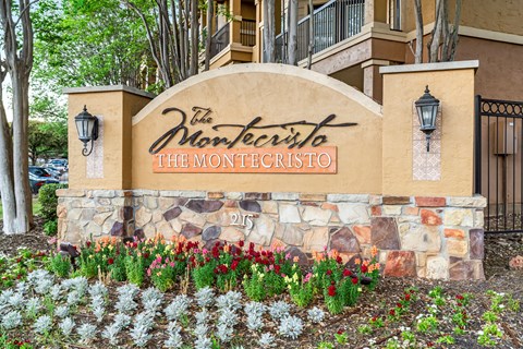 The Monte Cristo sign is in front of a building and has flowers in front of it.