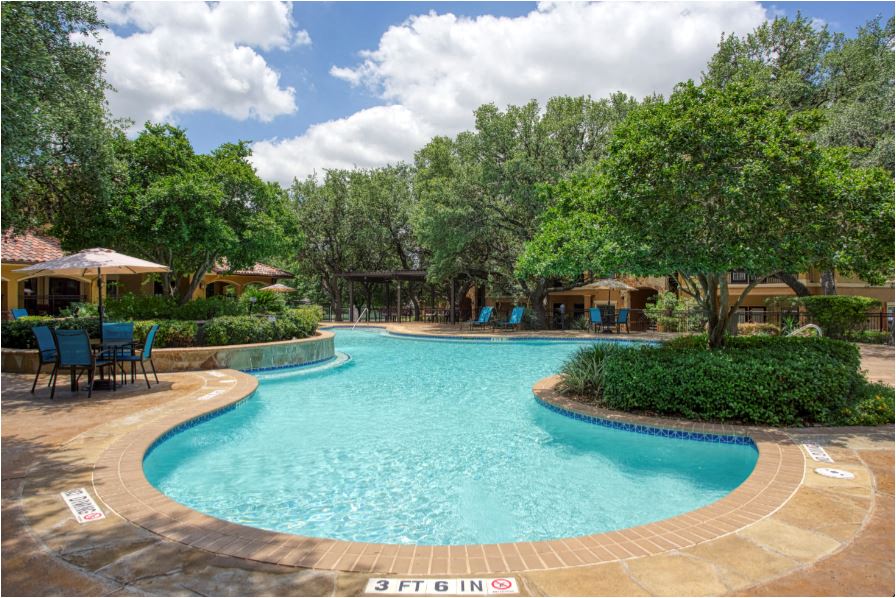 a large swimming pool with tables and umbrellas and trees