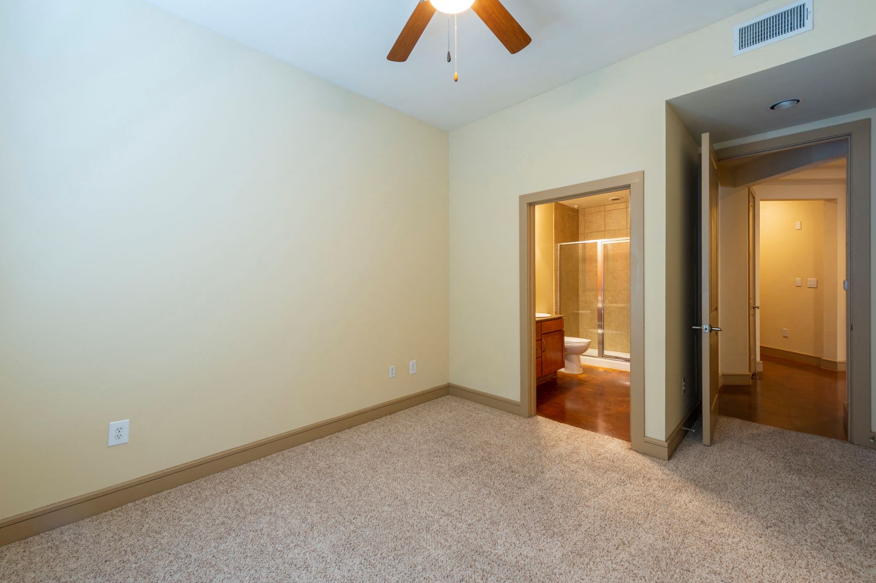 a empty living room with a ceiling fan and a door to a bathroom
