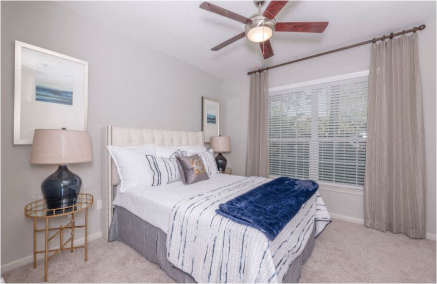 A bedroom with a bed, a ceiling fan, and a painting on the wall.